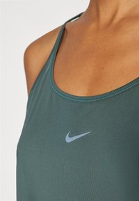 Sötétzöld, sima textúrájú Nike ujjatlan felső. Kerek nyakkivágással és egy világoskék Nike logóval rendelkezik elöl.