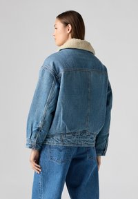 Veste en denim de couleur bleu clair avec un col en fausse fourrure. Présente une coupe décontractée, des détails de boutons et des poches poitrine, associée à un jean assorti.