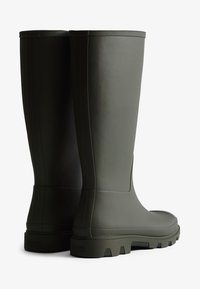 Bottes de pluie en caoutchouc vert avec une finition mate, tige haute pour une meilleure protection, semelles texturées et logo à l'arrière.