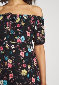 Sukienka odkrywająca ramiona z krótkimi bufkami, wykonana z teksturowanej czarnej tkaniny z kolorowymi kwiatowymi wzorami w różowym, niebieskim i żółtym kolorze.