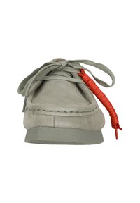 Chaussure en suède gris avec un bout arrondi, une semelle en caoutchouc lisse et des lacets gris présentant un accent rouge distinct d'un côté.
