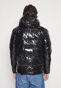 Černá prošívaná péřová bunda s lesklým povrchem, kapucí a vodorovným prošívaným vzorem. Má elastické manžety a spodní lem. Pohled zezadu.