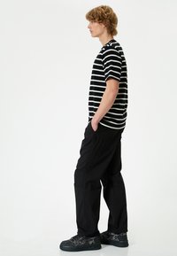 Sort og hvid stribet kortærmet skjorte, sorte cargo-bukser og sorte sneakers med teksturerede detaljer, vist fra siden.