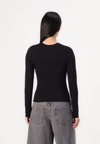Schwarzes Langarmoberteil mit rundem Halsausschnitt, kombiniert mit grauen, hochgeschnittenen Weitbeinhosen mit Gesäßtaschen und einer verblassten Textur.