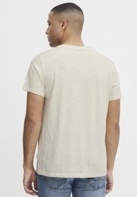 Camiseta de manga corta color beige claro, hecha de tela suave con un cuello redondo clásico, presenta un ajuste relajado y un diseño sencillo.