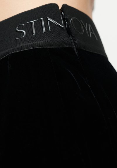 Fustă din catifea neagră, cu talie largă elastică și inscripție lucioasă „STINTOYA”, cu fermoar la spate.