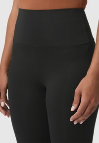 Hooggetailleerde zwarte leggings met een gladde textuur, voorzien van een brede tailleband en een aansluitend ontwerp. Geen zichtbare naden of hardware-details.