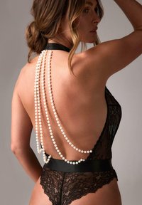 Czarny koronkowy body z głębokim wycięciem na plecach, z paskiem w talii i ozdobnymi białymi perełkami zwisającymi do dołu. Gładka faktura, przezroczysty design.
