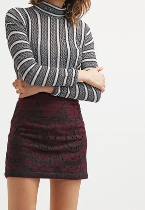 Cuello alto de rayas blancas y negras con falda burdeos con bordado negro intrincado y detalles recortados. Textura suave, diseño ajustado.