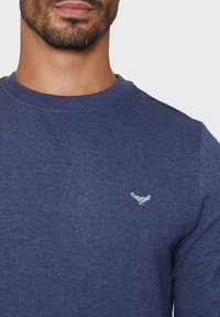 Marineblauwe katoenen sweatshirt met een ronde halslijn, subtiele textuur en een klein geborduurd logo op de borst.