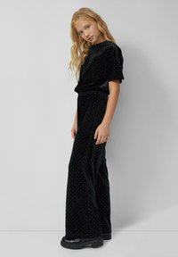 Zwarte fluwelen jumpsuit met zilveren stippen, voorzien van een top met korte mouwen en brede pijpen, gecombineerd met stevige zwarte platformlaarzen.