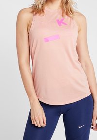 Helles rosa Tanktop aus Baumwolle mit rundem Ausschnitt, das ein auffälliges, kontrastierendes lila "NKE"-Textdesign auf der Vorderseite aufweist.
