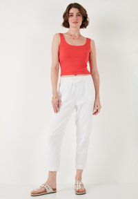 Rode getailleerde tanktop, witte joggingsbroek met rafelige omslagen en versierde sandalen. Casual outfit met een comfortabele pasvorm.
