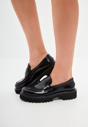 Black patent leather loafers with a chunky sole, featuring a flat heel and decorative stitching on the upper. Smooth texture and slip-on design.