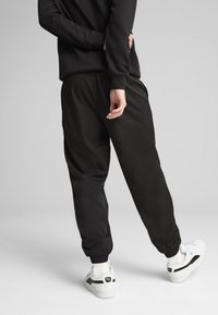 Sorte træningsbukser med elastiske manchetter, der har en glat tekstur. Sat sammen med hvide sneakers, der har accenter i farver og logo-detalje.