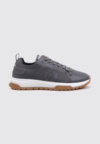 Zapatillas deportivas grises con parte superior de malla, suela de goma y una suela de tracción marrón en contraste. Incluyen un diseño de cordones y un detalle de logo en el lado.