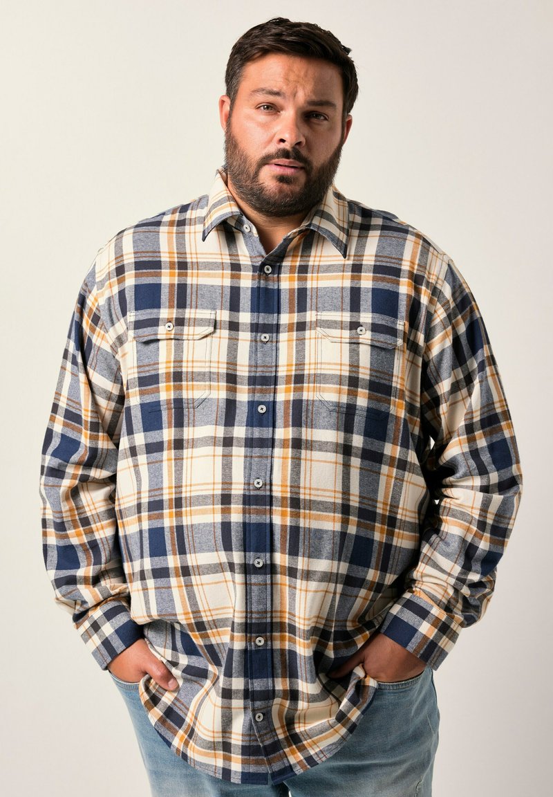Camicia in flanella con motivo a quadri nei colori blu navy, bianco e senape. Maniche lunghe, chiusura con bottoni e due tasche sul petto. Tessuto misto cotone.