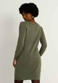 Vestido de punto en verde oliva con mangas largas, cuello redondo, forma ajustada y textura de brillo sutil. Sin patrones ni acentos visibles.