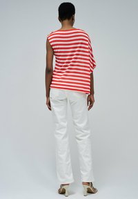 Top de rayas rojas y blancas de manga corta con un corte holgado, combinado con pantalones rectos blancos y sandalias de color claro.