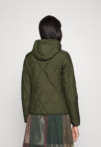 Olivengrøn quiltet jakke med hætte, der har buede syninger og en slim fit, kombineret med en multicolorer gennemsigtig nederdel.