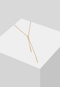 Guldfarvet lagdelt halskæde med en central knude og to hængende ender, lavet af en glat metal kæde. Enkelt, minimalistisk design.