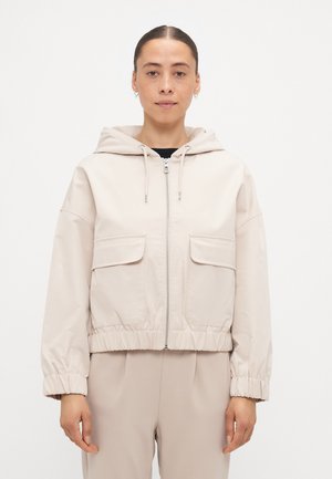 Heleda beez värvi lühikese lõikega jope kapuutsiga, ees lukuga, elastsete äärtega ja kahe suure taskuga. Sile tekstuur ja minimalistlik disain.