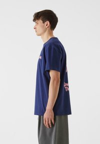 Mörkblå bomullströja med korta ärmar, med rosa grafisk text på framsidan och baksidan. Klassisk rund halsdesign.