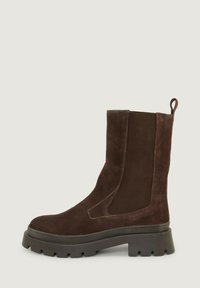 Brune suede ankelstøvel med elastiske sidestykker og en trekkflik, med en kraftig svart gummisåle og kontrasterende sømdetaljer.