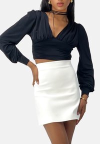 Zwarte wikkeltrui met lange mouwen en pofmouwen, gecombineerd met een witte mini-rok. De top heeft een diepe V-hals en geplooide details.