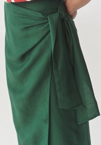 Falda envolvente verde con tejido suave y texturizado, un lazo en la cintura y una abertura lateral para mayor detalle.