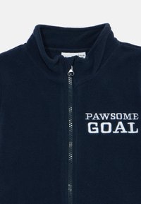 Marineblauwe fleecejack met een hoge kraag, een rits aan de voorkant en witte geborduurde tekst met "PAWSOME GOAL" aan de linkerkant.