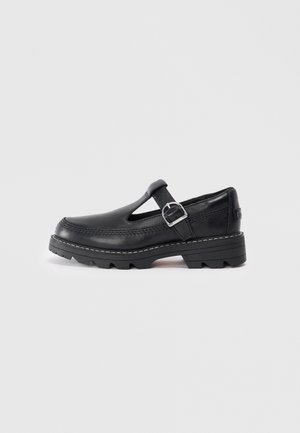 Black leather shoe with a T-strap design and buckle, featuring stitched detailing and a chunky textured sole for durability.