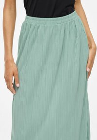 Midi-hame pleidattu pehmeässä mintunvihreässä värissä. Sisältää joustavan vyötärön ja kevyttä materiaalia, jossa on virtaava ja teksturoidun näköinen pinta.