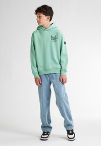 Felpa con cappuccio verde menta e tasca a canguro con grafica di montagne nere. Abbinala a jeans a gamba dritta blu chiaro e sneakers nere.