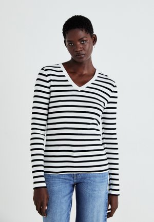 Haut à rayures noir et blanc à manches longues avec un décolleté en V, fabriqué en tissu doux et extensible ; associé à un jean bleu clair.