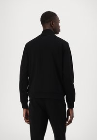 Schwarzer Kapuzenpullover mit hohem Kragen, gerippten Bündchen und Saum. Der glatte Stoff zeigt ein minimalistisches Design ohne sichtbares Logo oder Muster.