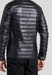 Sort polstret jakke med horisontal quiltning, skinnende stof og lange ærmer. Har en rund halsudskæring og slim fit.