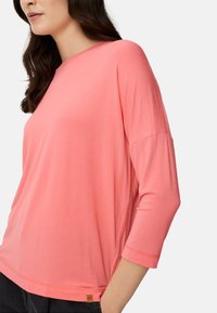 Koralfarvet, let, langærmet top med afslappet pasform, bred halsudskæring og en detalje med mærke ved kanten. Blød tekstur og let stretch.