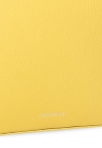 Portafoglio in pelle gialla con finitura testurizzata, caratterizzato da cuciture sottili e un logo in rilievo argentato, Coccinelle, sul fronte.