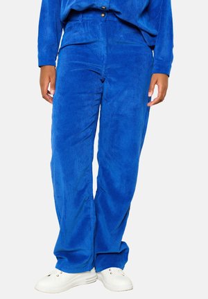 Blue corduroy pants with a straight cut, featuring vertical stripes, a button closure, and side pockets, paired with white sneakers.