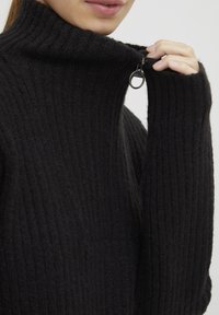 Maglione nero a coste con colletto alto, caratterizzato da una zip sul collo e maniche leggermente oversize per un fit rilassato.