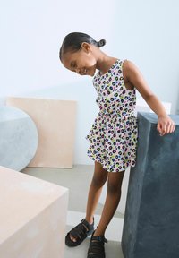 Weißes Kleid mit buntem Leopardenmuster, geraffter Taille und ausgestellt Rock. Schwarze Riemchensandalen. Neutrale geometrische Hintergrund.