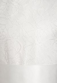 Bílé šaty s květinovou krajkovou texturou na horní části a hladkou saténovou sukní. Podrobné květinové vzory v jemném reliéfu.