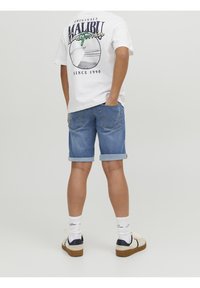 Camiseta blanca con un gráfico de "Malibu California", pantalones cortos de mezclilla azules con los puños doblados, calcetines blancos y zapatillas deportivas con detalles en azul marino.