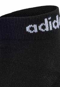 Czarna sportowa skarpeta o ryflowanej teksturze z białym logo tkanym w pobliżu górnej krawędzi. Projekt charakteryzuje się wyraźnym, dopasowanym kształtem kostki.