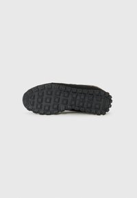 Black athletic shoe sole with a textured tread pattern and square grooves for traction. Durable rubber material, designed for grip on various surfaces.