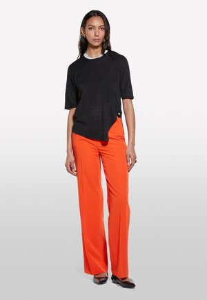 Black short-sleeve top with white neckline, paired with orange wide-leg trousers and black shoes. Smooth fabric, minimalist design, notable color contrast.