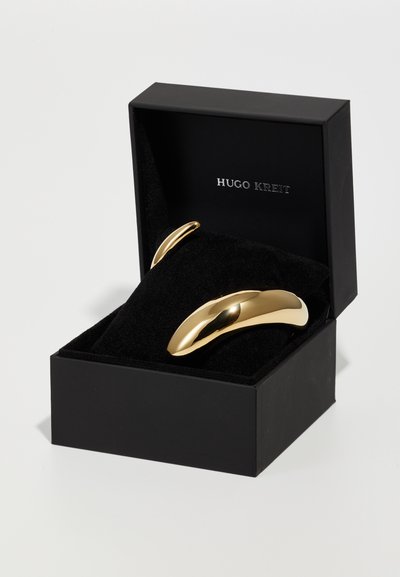 Gold-toned metal cufflinks with a smooth, curved shape, presented in a black box lined with black velvet. Logo reads "HUGO KREIT."
