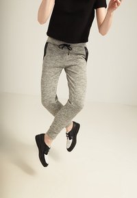 Grå joggingbukser med sorte sidelommer og justerbar snor. Båret med sorte og hvide sportsko. Glat, strækbart stof.