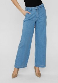 Jean large bleu clair en denim, avec une taille à boutons, des passants de ceinture et des poches latérales. Texture lisse avec une finition soignée.